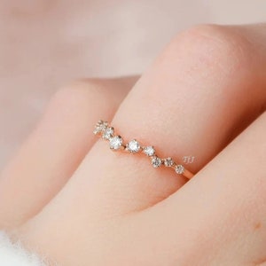 Könnte beinhalten: Ein zarter Roségold-Bandring mit einer geschwungenen Linie aus kleinen, funkelnden Diamanten.