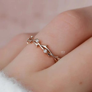 May include: A delicate rose gold ring with a vine design and small clear stones. The ring is on a finger.