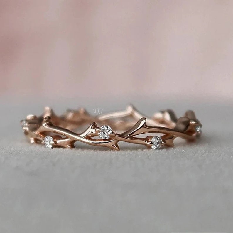 May include: A delicate rose gold ring with a twig design and small clear stones.