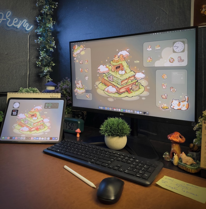 May include: A computer monitor and a tablet displaying a matching digital illustration of cats on a stack of books. The setup includes a black keyboard, a black computer mouse, a white stylus, a small potted plant, and decorative mushroom figurines.