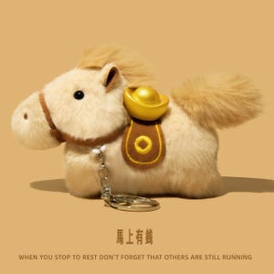 Puede incluir: Un llavero de peluche con forma de caballo crema, con una silla de montar dorada y un lingote de oro. El caballo tiene una melena y cola esponjosas, y un llavero de metal. El texto en la parte inferior dice: "WHEN YOU STOP TO REST DON'T FORGET THAT OTHERS ARE STILL RUNNING."