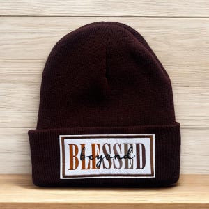 May include: A maroon beanie with a white patch that says "Blessed beyond" in brown, orange, and white lettering.