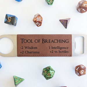 May include: A brown leather bottle opener with a metal opener on one end. The bottle opener has the text "TOOL OF BREACHING" and the following stats: "-2 Wisdom +2 Charisma -1 Intelligence +2 vs bottles". The bottle opener is surrounded by various colored dice.