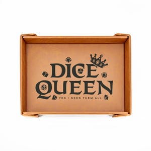 May include: A brown leatherette dice tray with the words "DICE QUEEN" in black, along with dice graphics and a crown. The text "YES I NEED THEM ALL" is below the main text. The tray has a rectangular shape with raised edges.