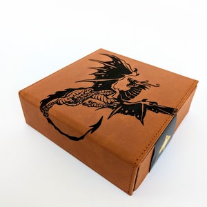 May include: A brown leather box with a black dragon design on the top. The box has a black and gold trim.