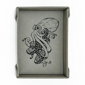 May include: A gray, rectangular dice tray with a black octopus illustration. The tray has a stitched border and four corner tabs. The octopus design includes dice with numbers.