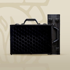 Pode incluir: Duas malas pretas de casco rígido com um padrão de favo de mel na frente. A mala à esquerda tem uma alça na parte superior. A mala à direita tem uma alça lateral.