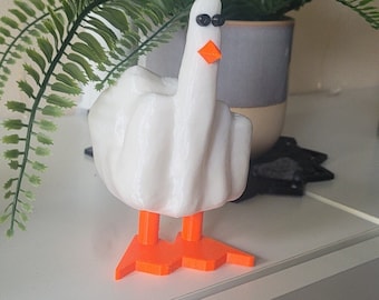 May include: A white, 3D-printed goose figurine with an orange beak and feet, and black eyes. The goose is giving the middle finger. The figurine is a humorous decorative item.
