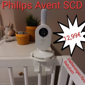 Może przedstawiać: Biały monitor dla dziecka z obiektywem kamery i logo Philips Avent. Monitor jest zamontowany na białym łóżeczku z białym i szarym pikowanym ochraniaczem. Monitor kosztuje 12,99 euro. Tekst "Halterungen für Babybett" jest widoczny po prawej stronie obrazu. Tekst "Variante 1" jest widoczny na dole obrazu.
