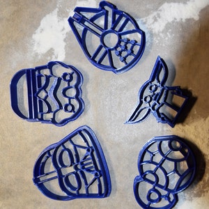 Puede incluir: Cinco cortadores de galletas de plástico azul con forma de personajes de Star Wars: Darth Vader, Yoda, un Stormtrooper y dos versiones del Halcón Milenario.