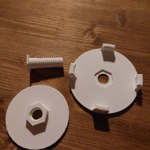 May include: White plastic parts for a 3D printed project, including a screw, a round disc with a hole in the centre and four tabs, and a flat disc with a hexagonal hole in the centre. The text "Variante 2" is visible in the image.