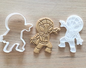 May include: Three cookie cutters, two are white and one is brown. The brown cutter is shaped like a cartoon superhero wearing a red and blue suit. The white cutters are shaped like the same superhero, one is standing and the other is in a crouching pose.