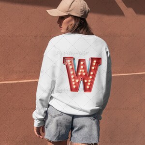 May include: White sweatshirt with a large, red letter "W" on the back. The letter is designed to look like a vintage marquee sign, with small, round, yellow lights. The sweatshirt is paired with denim shorts and a tan baseball cap.