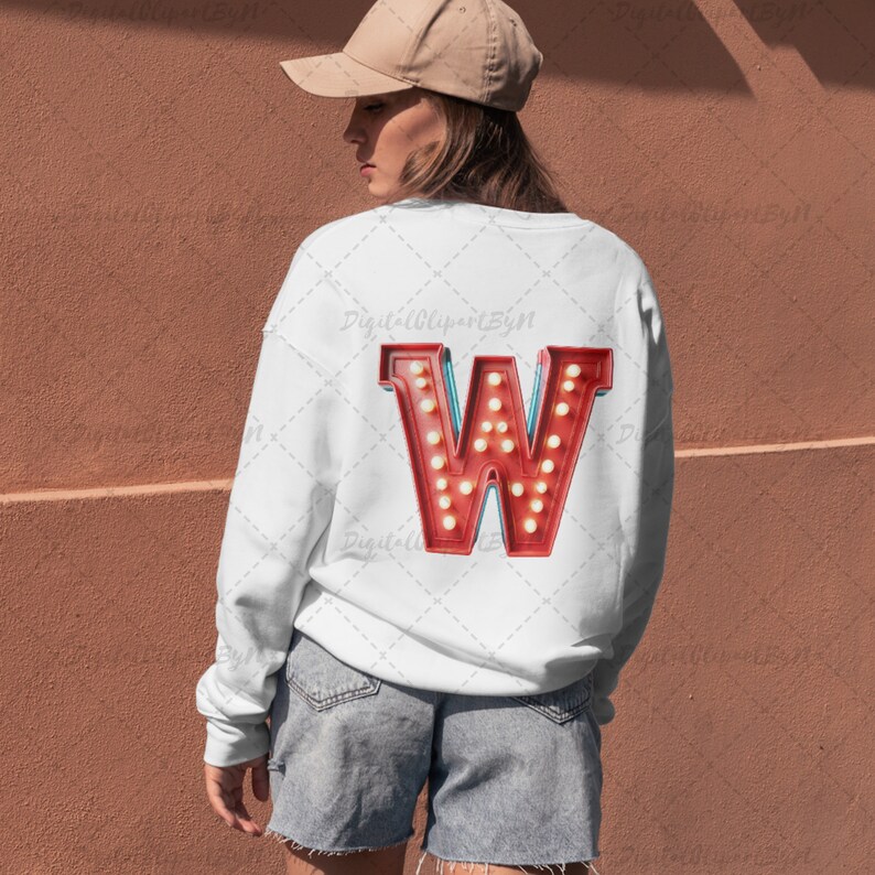 May include: White sweatshirt with a large, red letter "W" on the back. The letter is designed to look like a vintage marquee sign, with small, round, yellow lights. The sweatshirt is paired with denim shorts and a tan baseball cap.