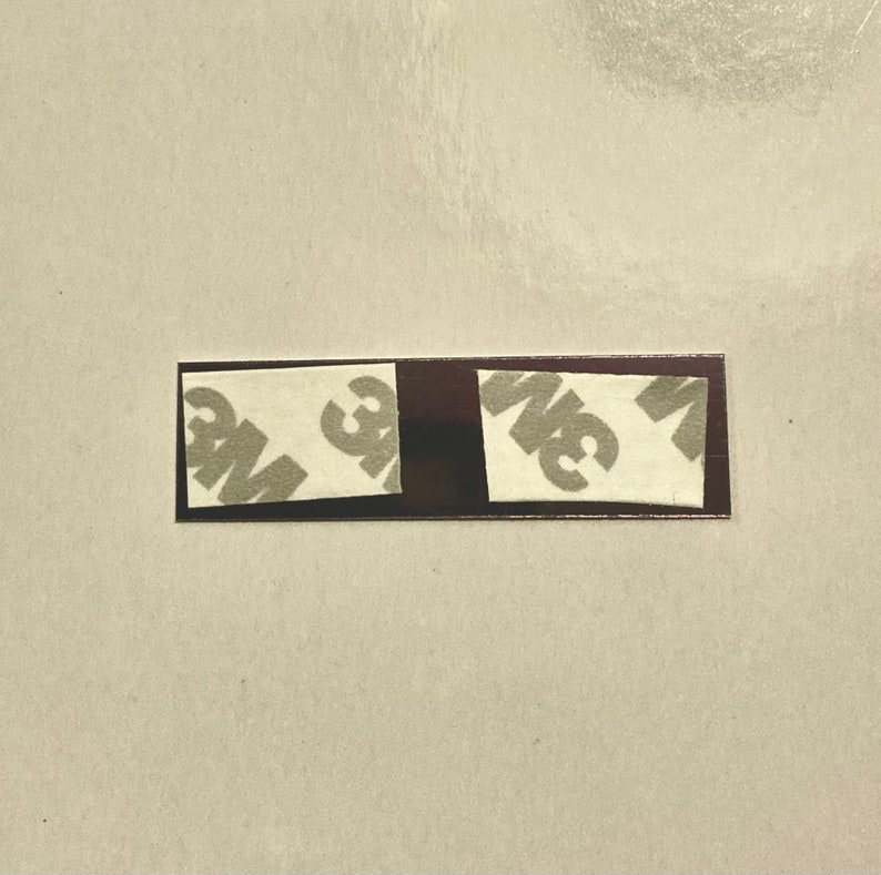 May include: Two small, rectangular pieces of brown tape with white adhesive backing. The tape has the 3M logo printed on it.