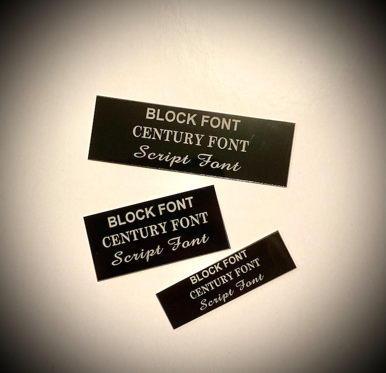 May include: Three black rectangular name tags with white text. The text on each tag reads "BLOCK FONT", "CENTURY FONT", and "Script Font".