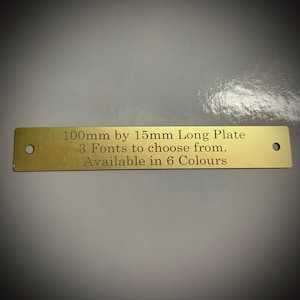 Può includere: Una piastra rettangolare in ottone con due fori, con testo inciso. Il testo recita: "100 mm per 15 mm Long Plate, 3 font tra cui scegliere, Disponibile in 6 colori."