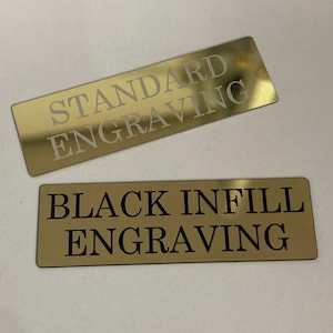K&ouml;nnte beinhalten: Zwei rechteckige, goldfarbene Metallplatten mit graviertem Text. Die obere Platte tr&auml;gt die Aufschrift "STANDARD ENGRAVING" in heller Farbe. Die untere Platte tr&auml;gt die Aufschrift "BLACK INFILL ENGRAVING" in Schwarz.