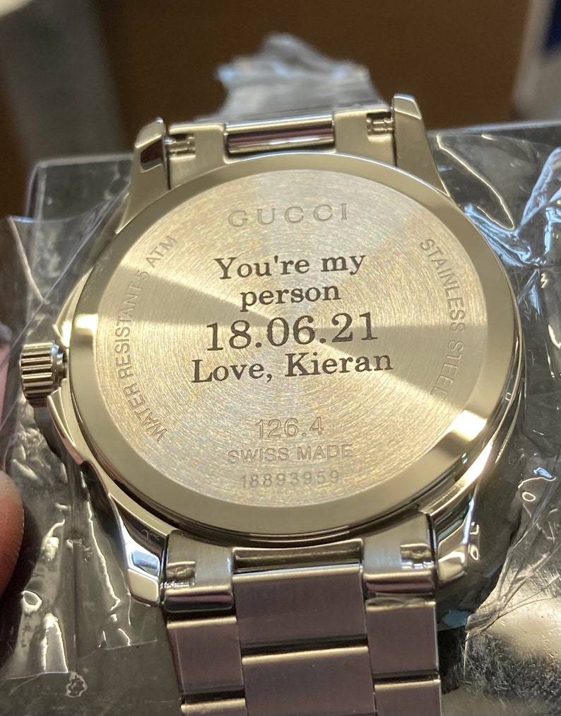 Pu&ograve; includere: Un orologio Gucci argentato con cinturino in acciaio inossidabile. Il retro dell'orologio &egrave; inciso con il testo "You're my person 18.06.21 Love, Kieran" e "126.4 SWISS MADE 18893959".
