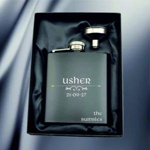 Può includere: Una fiaschetta nera con la parola "usher" e la data "21-09-27" incisa sul davanti, presentata in una scatola nera con fodera in raso. È incluso un piccolo imbuto. Le parole "the bumbles" sono incise anche sulla fiaschetta.