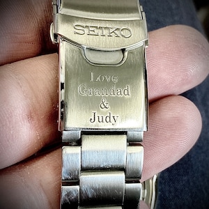 Pu&ograve; includere: Un cinturino da orologio in metallo argentato con le parole "SEIKO", "Love Granddad & Judy" incise sulla fibbia.