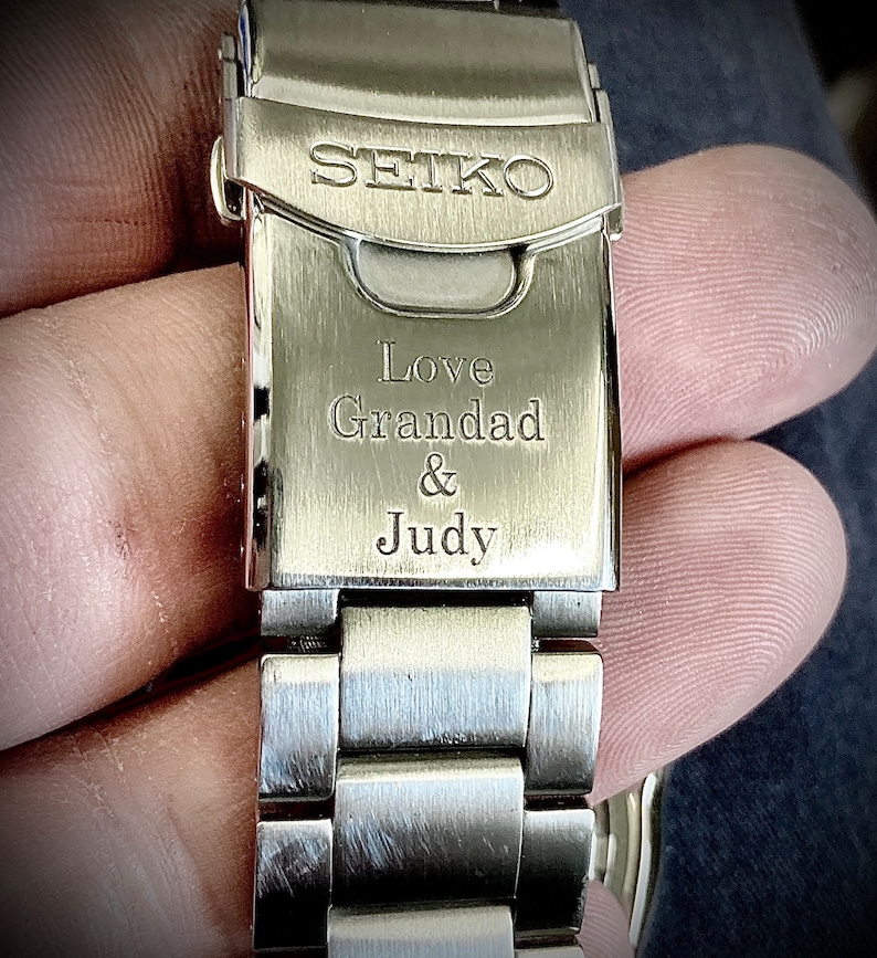 Pu&ograve; includere: Un cinturino da orologio in metallo argentato con le parole "SEIKO", "Love Granddad & Judy" incise sulla fibbia.