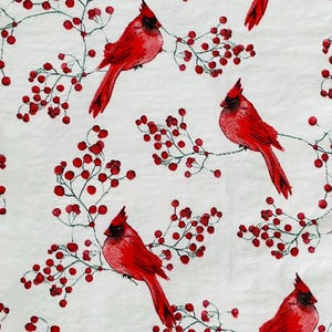 May include: White background with a repeating pattern of red cardinals perched on branches with red berries. The birds have a distinctive crest and long tails. The berries are small and round, adding a festive touch.