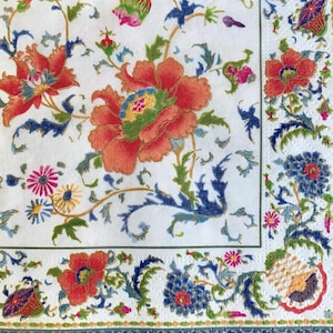 May include: A white fabric napkin with a floral design. The design features red, orange, blue, green, and yellow flowers. The flowers are arranged in a repeating pattern on a white background.