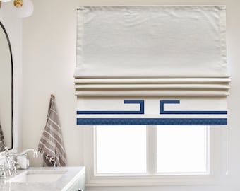 May include: White roman shade with a blue and white geometric pattern border. The shade is raised and the cord is visible.
