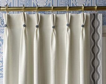 May include: White curtains with pleats and gray button accents hanging from a gold rod against a blue and white patterned wallpaper.