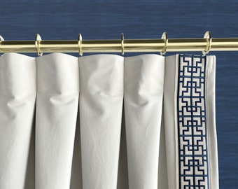 May include: White curtains with a geometric pattern border in navy blue. The curtains are hung on a gold rod.
