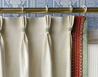 May include: White linen curtains with a decorative trim in shades of orange and green. The curtains are hung on a gold rod with decorative finials.