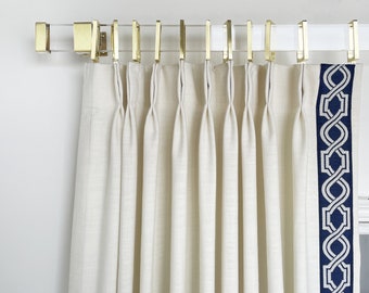 May include: White curtains with a navy blue geometric pattern along the edge, hanging from a gold curtain rod with clear acrylic finials.