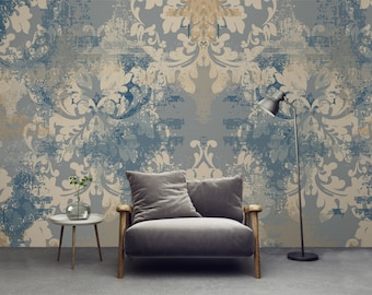 May include: A gray armchair with wooden arms sits in front of a wall with a blue and beige damask pattern. A small table with a vase of green plants sits next to the chair. A floor lamp with a black shade stands to the right of the chair.