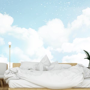 May include: A white bed with white bedding and a white headboard is in front of a wall mural depicting a blue sky with white clouds and white stars.