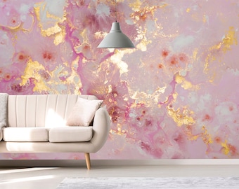 May include: A pink and gold abstract art wallpaper with a cream-colored sofa and a gray pendant light. The wallpaper features a fluid design with gold accents and a soft, dreamy aesthetic. The sofa has a throw blanket and a pillow.