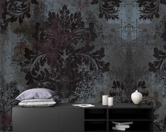 May include: A black media console with four shelves, featuring a distressed damask pattern wallpaper backdrop. The console has a white ceramic vase and two white ceramic candle holders on top.