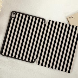 May include: Black and white striped iPad case with a black border. The case is open and lying flat on a white surface.