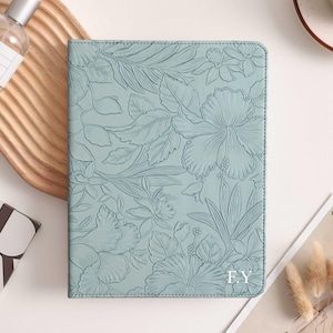May include: A light blue journal with a floral embossed design. The cover features a detailed pattern of flowers and leaves. The initials "FY" are embossed in the lower right corner. The journal is rectangular and appears to be made of leather.
