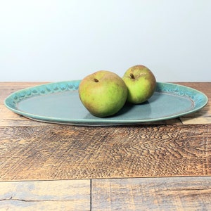May include: A light blue oval ceramic serving platter with two green apples on top.