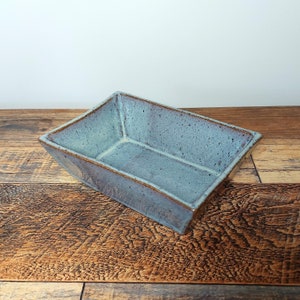 May include: A light blue ceramic rectangular dish with a speckled glaze. The dish is sitting on a wooden surface.