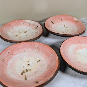 May include: Four small, round ceramic bowls with a pink and white glaze. The bowls have a speckled, textured surface and a slightly uneven rim.