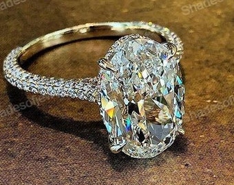 Può includere: Un anello di fidanzamento in oro con un grande diamante ovale incastonato in pavé. L'anello è su una superficie marrone.