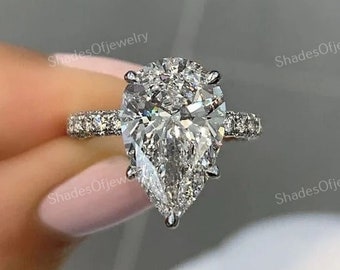 Può includere: Un anello di fidanzamento con diamante a forma di pera con una montatura a halo. L'anello è in oro bianco e presenta una fascia pavé.