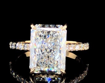 May include: A radiant cut diamond engagement ring with a gold band and a pave setting. The ring is set on a black background.