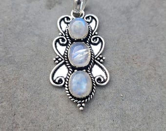 May include: A silver-toned pendant featuring three oval moonstone cabochons. The pendant has an ornate, filigree design with a bail at the top for a chain. The moonstones have a milky, iridescent quality, set in a decorative, vintage-style setting.