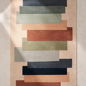 May include: Rectangular area rug with a beige background and a stacked design of various colored rectangles. The rectangles are in shades of blue, green, orange, and brown, creating a modern, geometric pattern.