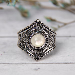 May include: A silver ring with an ornate design and a white mother-of-pearl stone in the centre.