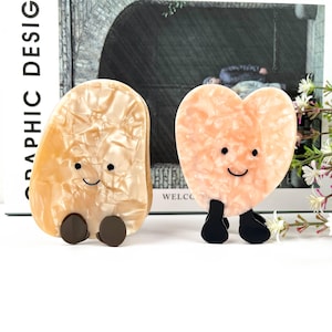 May include: Two small, colorful, resin figurines with happy faces and black legs. The figurine on the left is shaped like a pear and the figurine on the right is shaped like a heart.