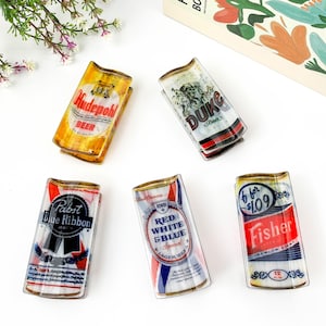 Peut inclure: Cinq plateaux rectangulaires en verre arborant des graphismes de canettes de bière vintage. Les motifs incluent les étiquettes Hudepohl, Duke, Pabst Blue Ribbon, Red White & Blue et Fisher. Chaque plateau présente un bord supérieur incurvé.